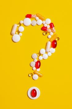 Home A creative arrangement of various pills forming a question mark against a bright yellow background.