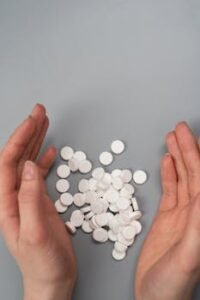 Home A close-up of hands surrounding white pills on a gray background, symbolizing medication and health concerns.